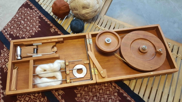 book-size charkha open with a piece of wool ready for spinning